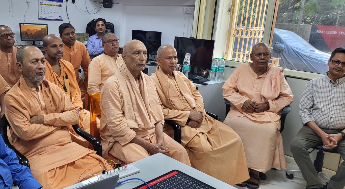 Senior monks of Bharat Sevashram Sangha seated in the lab watching a demonstration, with a breadboard and lit LEDs on the bench in front.