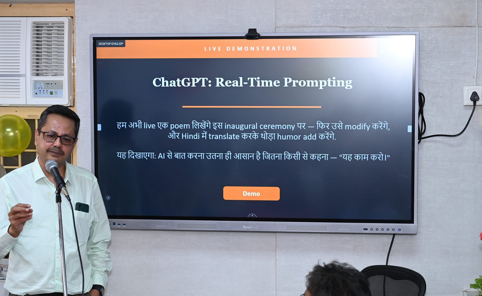 A volunteer presenting at the lab's teaching screen, which shows a live AI demonstration written in mixed Hindi and English.
