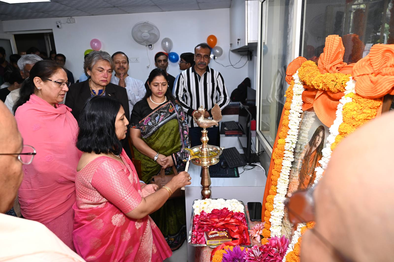 Guests lighting a ceremonial lamp beside a garlanded portrait, at the start of the inauguration.
